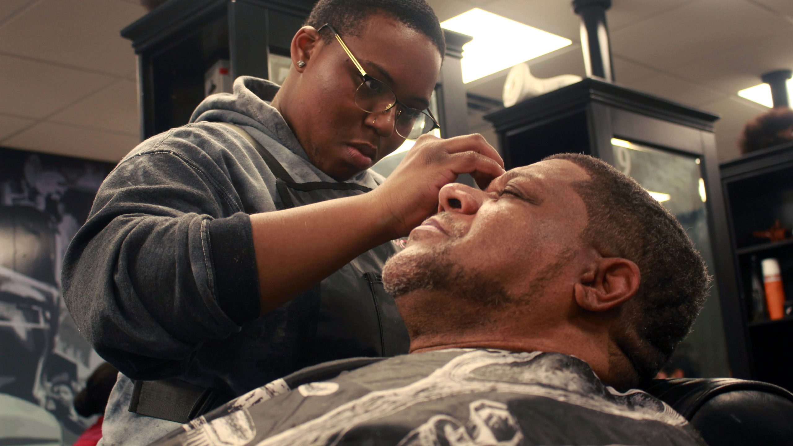 Student trims a customer's beard inside Barber College facility