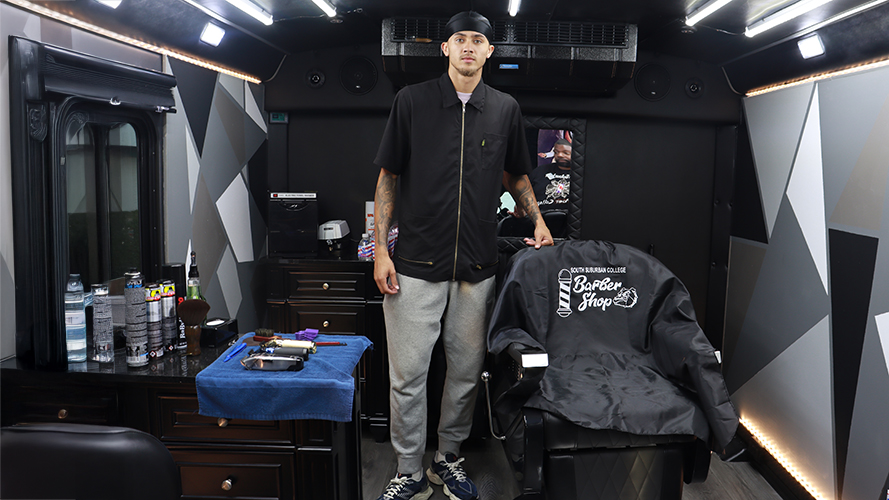 Student stands at chair inside mobile barber bus