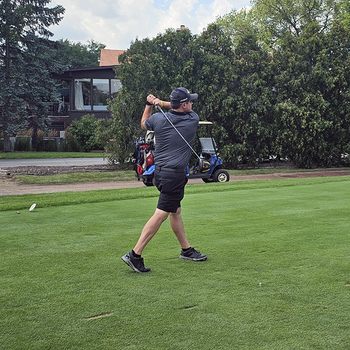 A golfer swings a golf club on a golf course.