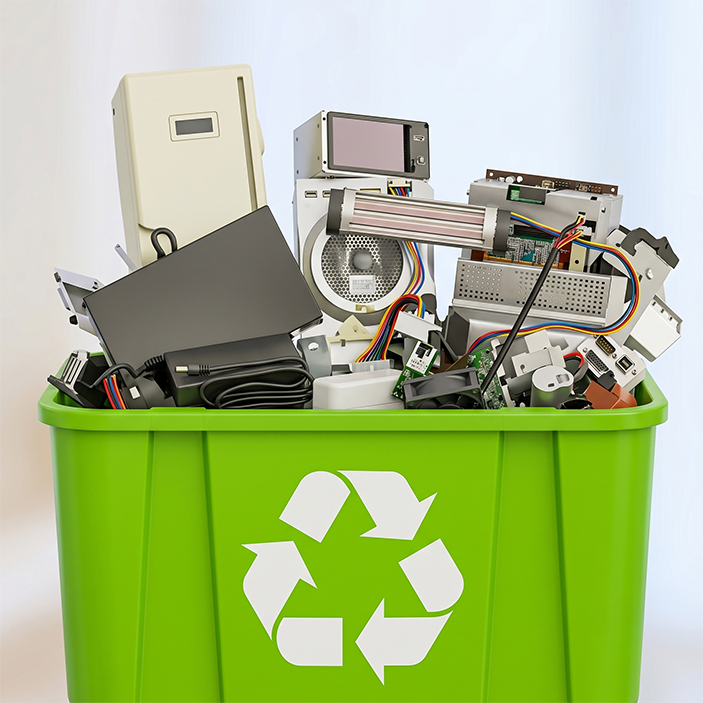 A bright green recycling bin featuring a white universal recycling symbol is filled to the brim with discarded electronic waste, including computer hardware, cables, and old monitors against a neutral background.